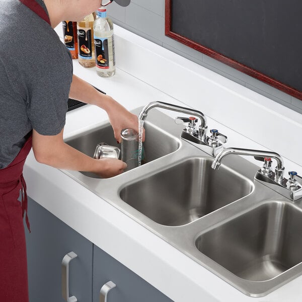 A person washing dishes in a Regency stainless steel three compartment drop-in sink.