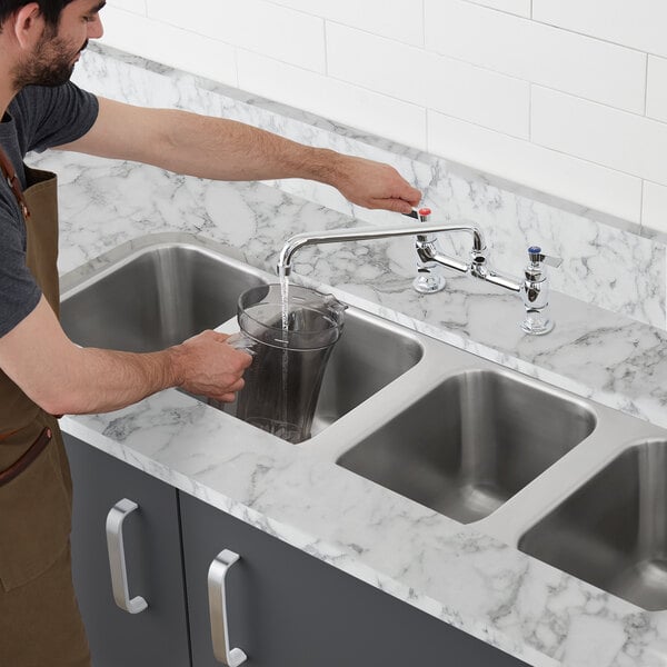 A man filling a glass with water from a stainless steel undermount sink.