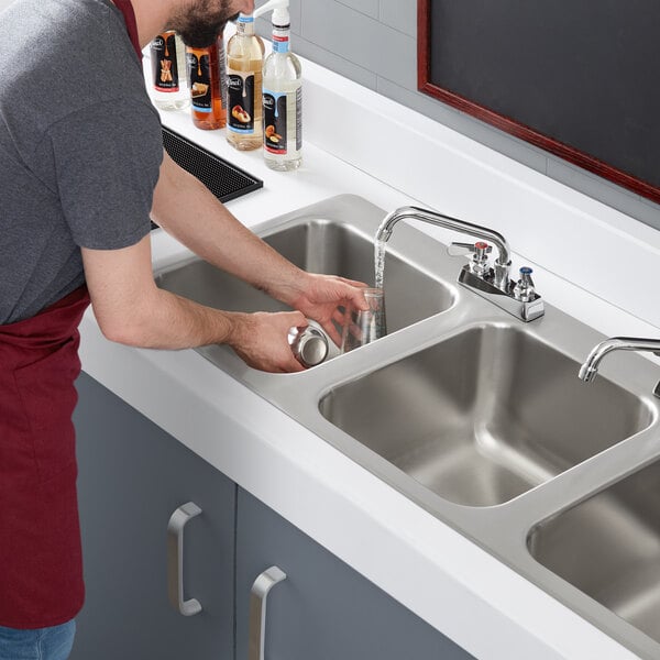 A man washing dishes in a Regency stainless steel drop-in sink.