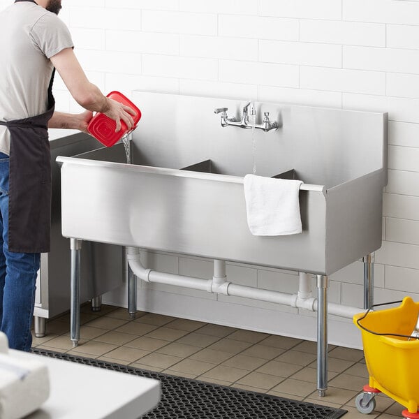 A man pouring water into a Regency stainless steel utility sink.