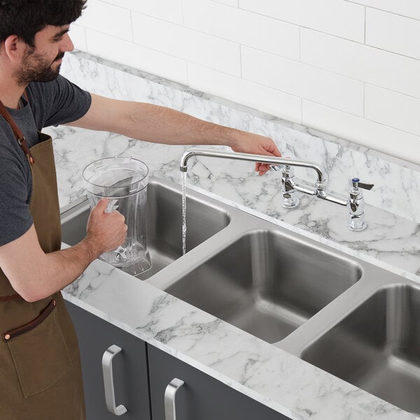 A man in an apron washing a glass in a Waterloo stainless steel undermount sink.