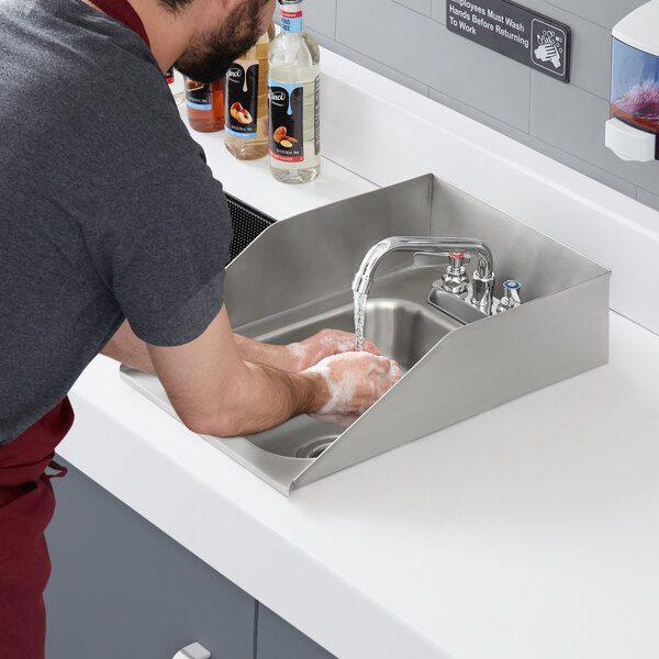 A man washing his hands in a Regency stainless steel drop-in sink with side splashes on a counter.
