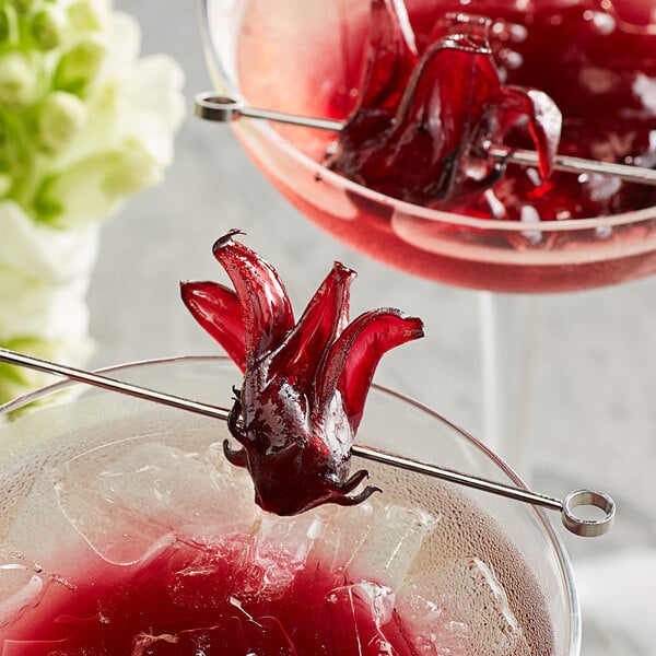 A close up of a glass with red liquid and ice with Wild Hibiscus flowers in it.