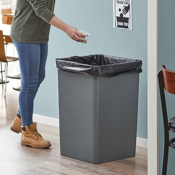 A woman standing next to a Lavex 35 gallon gray square trash can.
