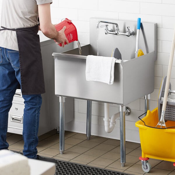A man in a black apron pouring water into a Regency commercial utility sink.