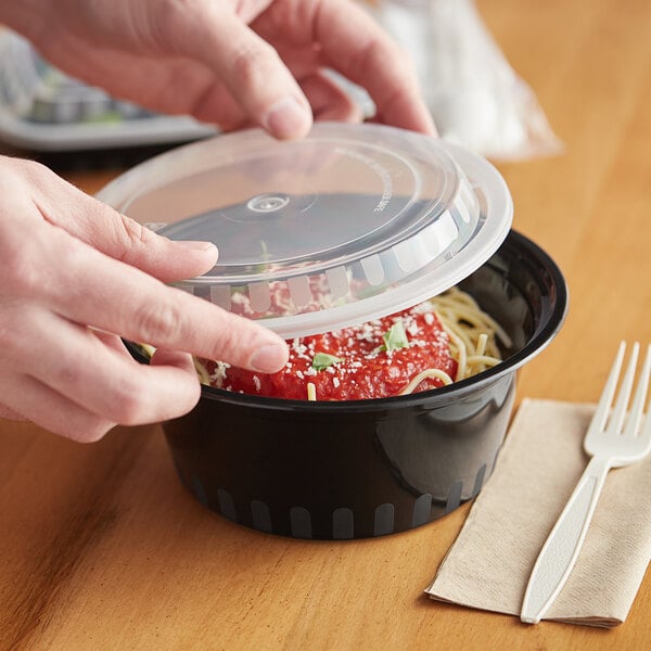 A person's hands putting spaghetti into a Choice black plastic container with a lid.