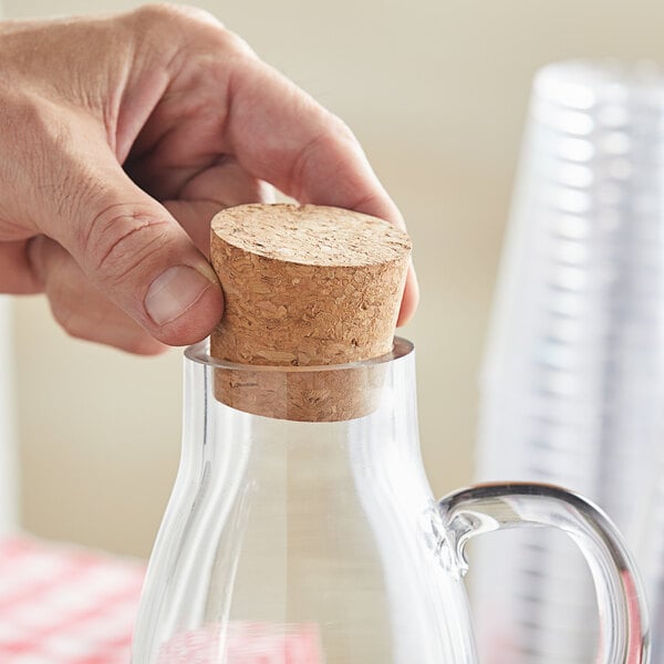 A hand using a cork to seal a glass pitcher.