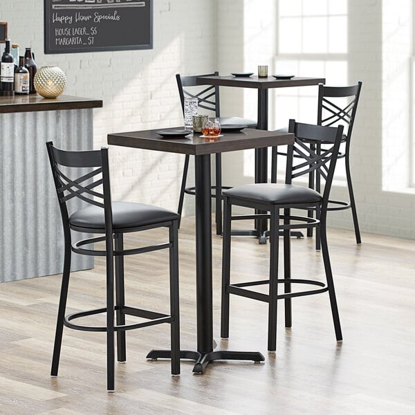 A Lancaster Table & Seating bar height table with a butcher block top and two chairs with black cushions.