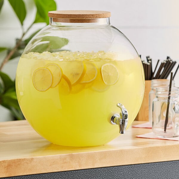 An Acopa fishbowl beverage dispenser with lemonade and lemons inside, with a cork lid and tap.