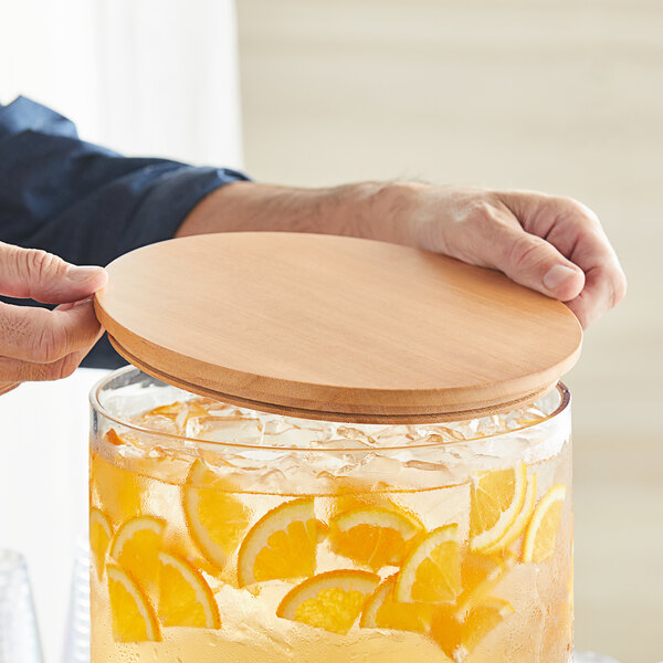 A person using a wooden lid to cover a glass container of ice and orange slices.