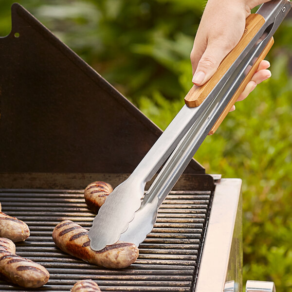A person using Outset stainless steel tongs to grill sausages.