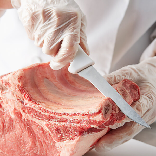 A person in white gloves using a Choice 5" Narrow Stiff Boning Knife to cut meat.
