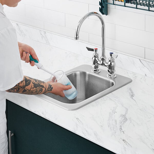 A person with tattoos on their arm washing a glass in a Waterloo drop-in sink.