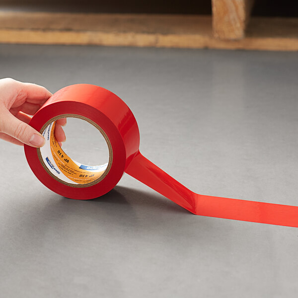A hand holding a roll of Shurtape red line set tape.