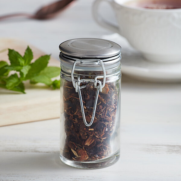 A Tablecraft glass condiment jar with a metal lid and clip filled with tea.