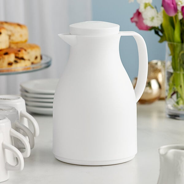 An Acopa white thermal carafe with a handle on a table with food.