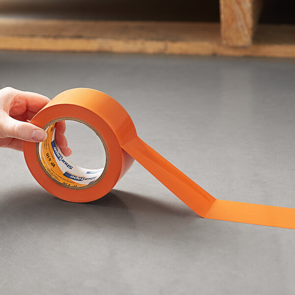 A hand holding a roll of Shurtape orange line set tape.