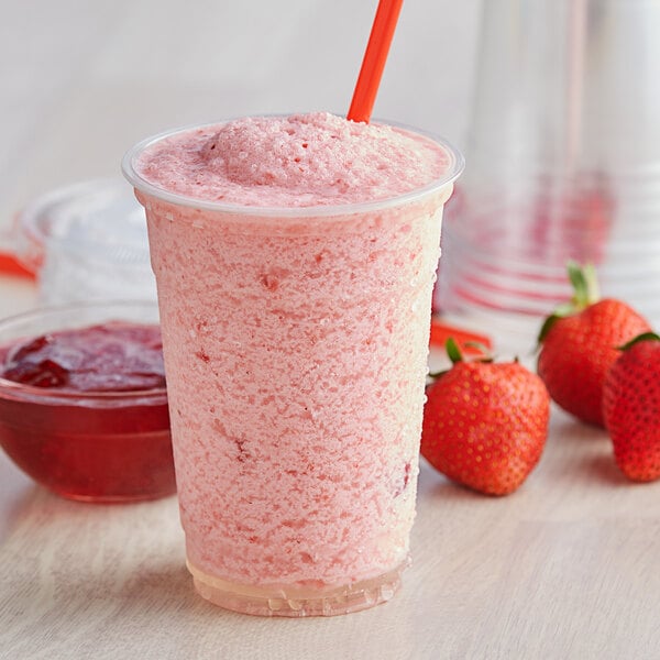 A plastic cup of strawberry smoothie next to strawberries.