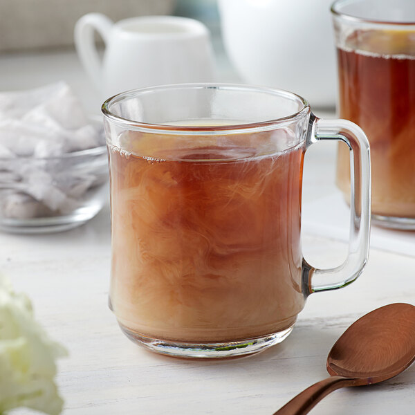 A glass mug of brown liquid with a spoon on the side.
