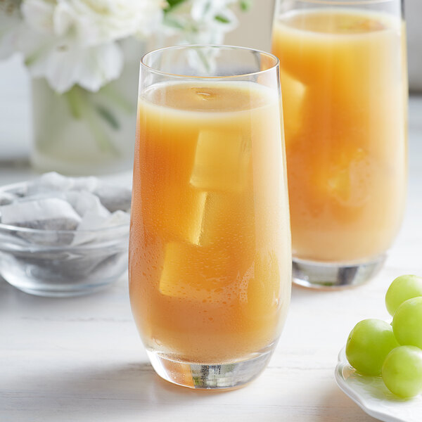 A glass of orange juice with ice cubes and grapes sitting next to a bowl of Bossen White Grape Oolong Tea Bags.