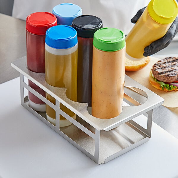 A person holding a metal Tablecraft squeeze bottle holder filled with yellow and blue containers of condiments.