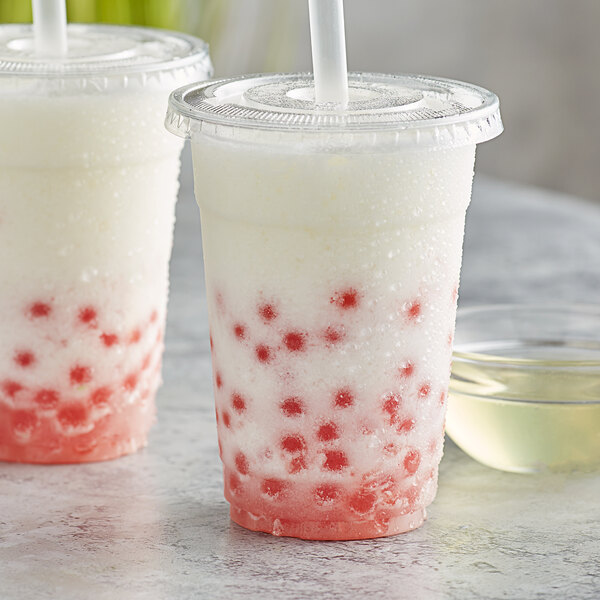 Two plastic cups with white lemon concentrate and red dots with straws.