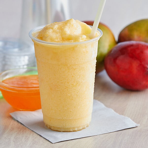 A yellow smoothie in a plastic cup with a straw and a spoon, made with Bossen Mango Fruit Jam.