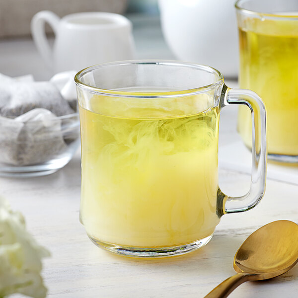 A glass mug of yellow Bossen Genmaicha tea with a gold spoon.
