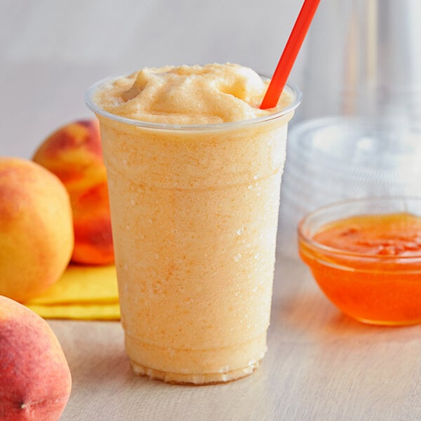 A cup of orange smoothie with a straw and a bowl of peach jam.