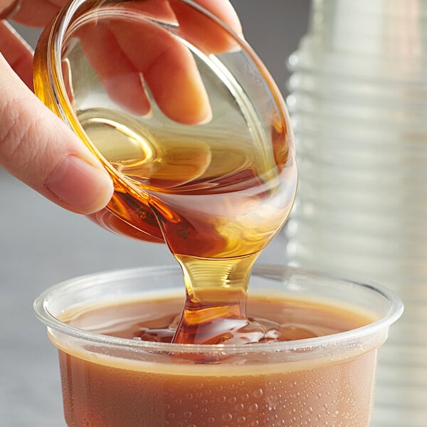 A hand pouring Bossen Honey Flavored Syrup into a cup of brown liquid.