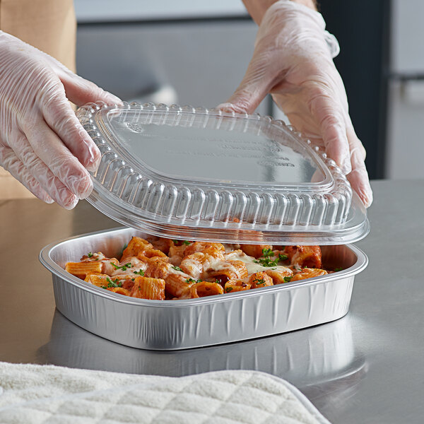 A gloved hand holding a ChoiceHD aluminum foil container of food.