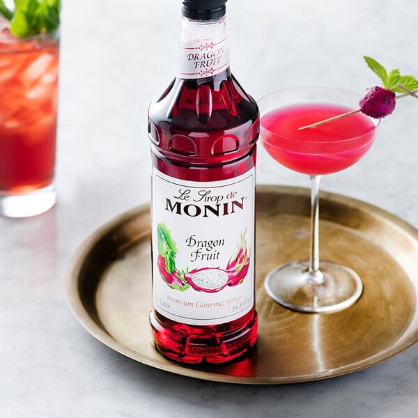 A close-up of a Monin bottle of red liquid next to a pink drink.