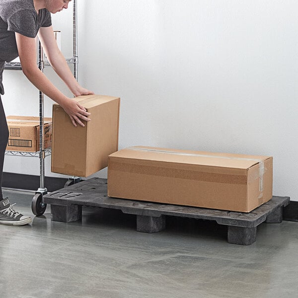 A person lifting a brown box onto a Lavex Modular Stackable Pallet Display Base.