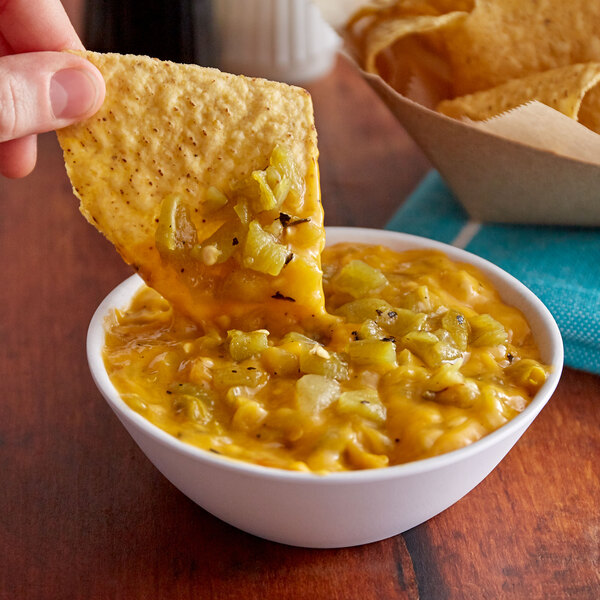 A person holding a tortilla chip and dipping it into a bowl of green chile peppers.