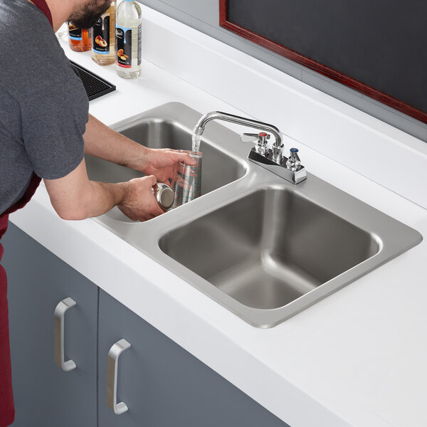 A man washing dishes in a Regency stainless steel drop-in sink with a swing faucet.