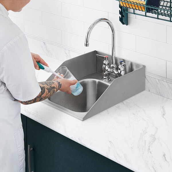A person washing dishes in a Waterloo stainless steel drop-in sink with a gooseneck faucet.