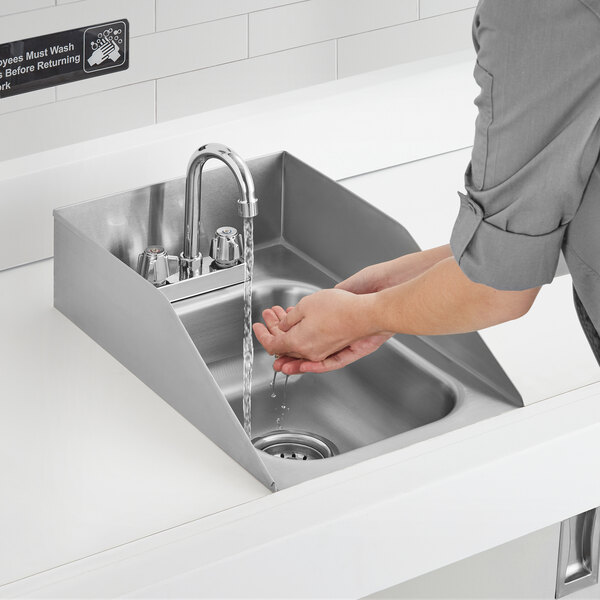 A person washing their hands in a Regency stainless steel sink with gooseneck faucet.