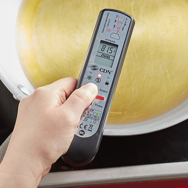 A hand holding a CDN ProAccurate digital infrared thermometer over a pan.