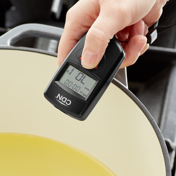 A person using a CDN Mini Digital Infrared Thermometer to measure the temperature of food in a pan on a kitchen counter.