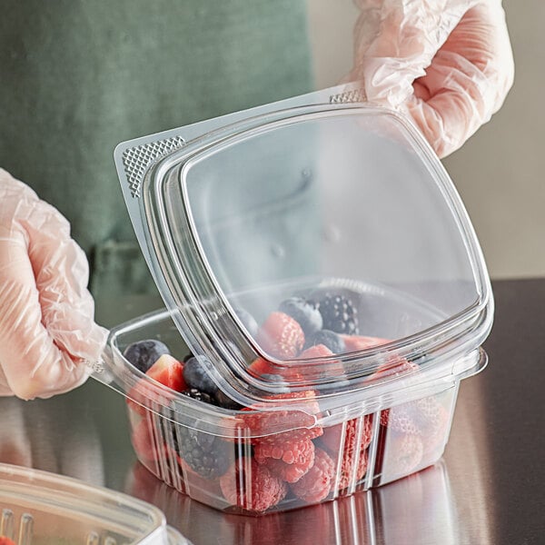 A person in gloves holding a Choice clear plastic deli container with berries.