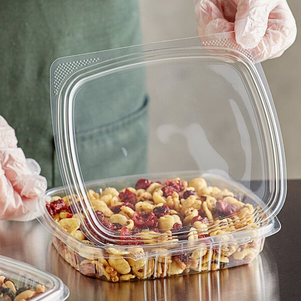 A gloved hand holds a Choice clear plastic deli container filled with food.