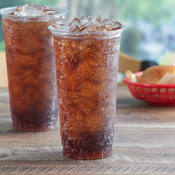 Two Choice clear plastic cups filled with ice tea on a table.