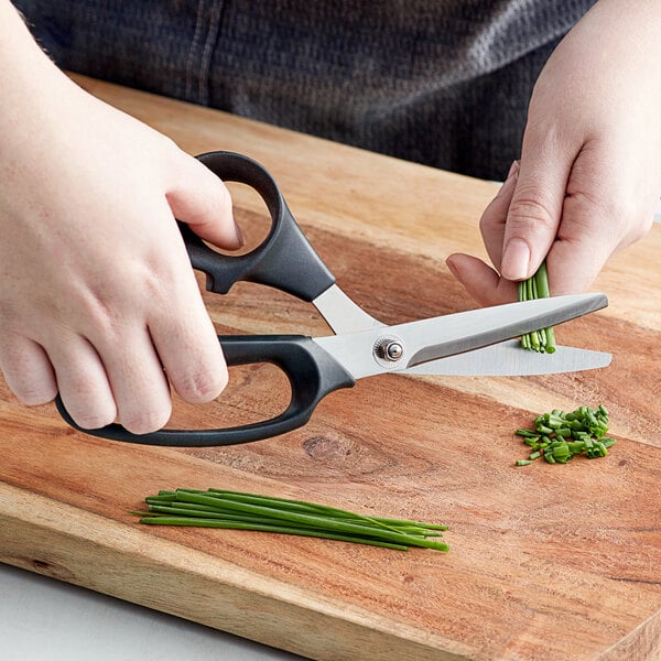 A person using Mercer Culinary kitchen shears to cut chives on a cutting board.