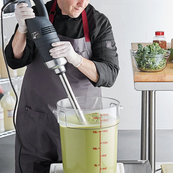A man in a chef's uniform using an AvaMix heavy-duty immersion blender to mix green liquid in a bowl.