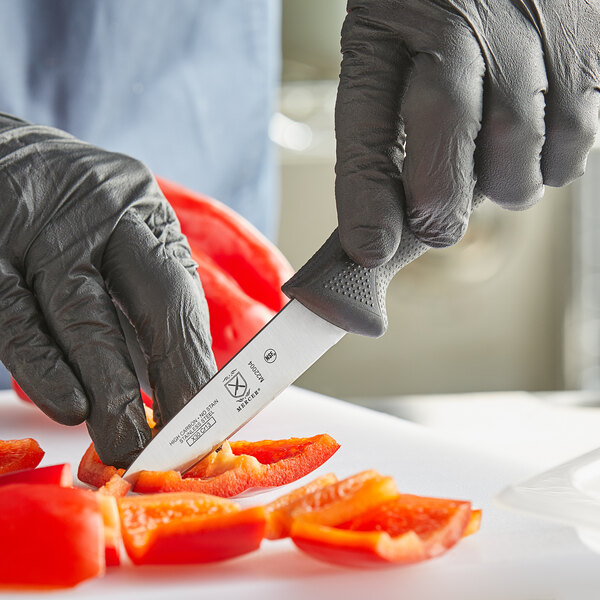 A person in black gloves uses a Mercer Culinary Millennia paring knife to cut a pepper.