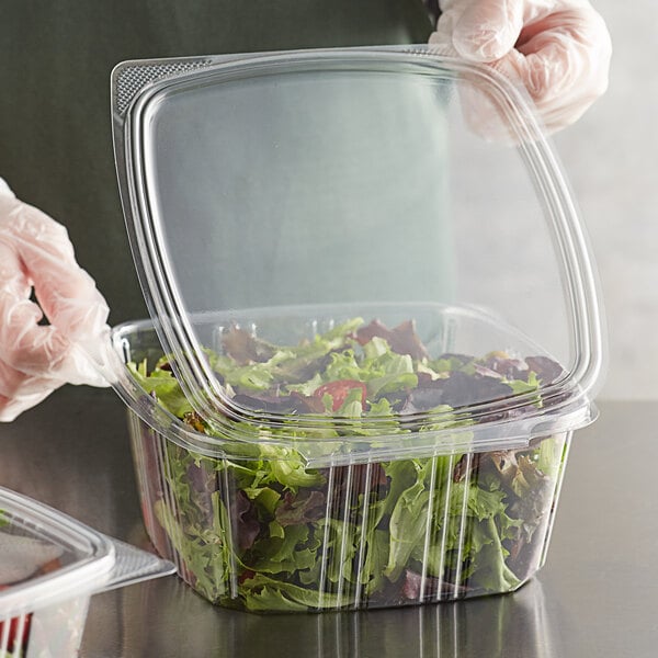 A gloved hand holds a clear plastic Choice deli container filled with salad.