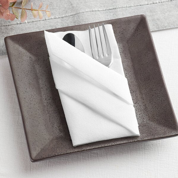 A white linen-like dinner napkin flat on a plate with a fork and knife.