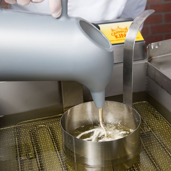 A person pouring funnel cake batter into a metal mold.