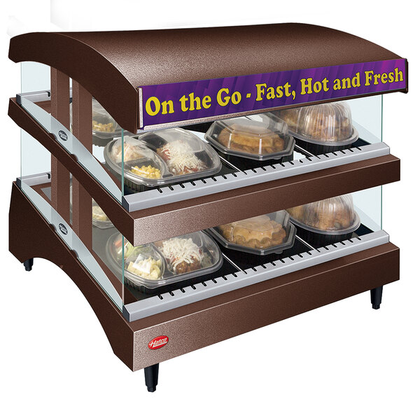 A Hatco countertop heated food display warmer with shelves of food in a bakery display case.