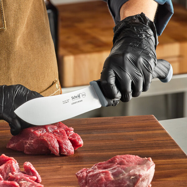 A person in black gloves using a Schraf Butcher Knife to cut raw meat on a wooden surface.